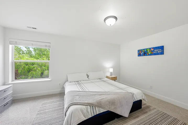 Bedroom with light gray carpeting, a large window, white walls, and a ceiling-mounted light fixture