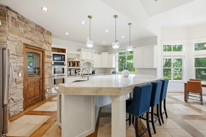 Spacious kitchen featuring an extended island with a light-toned countertop, white cabinetry, integrated stainless steel appliances, and a stone accent wall