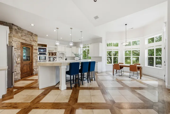 Spacious kitchen featuring white cabinetry, integrated stainless steel appliances, and an expansive center island with pendant lighting