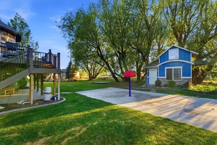 Expansive yard featuring a multi-level deck, concrete pad, and a separate blue outbuilding with a white entry door and stone façade
