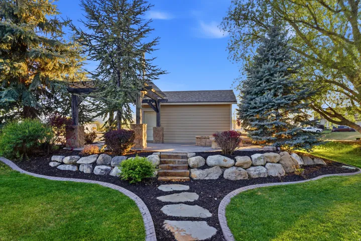 Outdoor patio featuring a pergola with brick and stone pillars, a stone retaining wall, and integrated landscaping