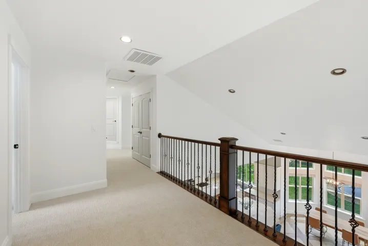 Upper level landing featuring light-toned carpeting, white walls, recessed lighting, and a dark wood and wrought iron railing overlooking the space below
