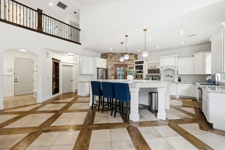 Open-concept kitchen featuring an expansive center island with seating, white cabinetry, integrated stainless steel appliances, and a tiled backsplash