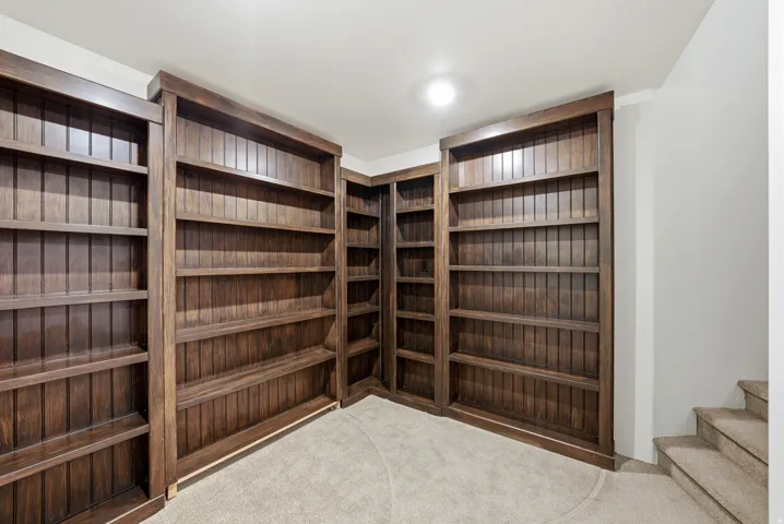 Built-in wood shelving units with beadboard backing, corner configuration, recessed ceiling lighting, and carpeted flooring
