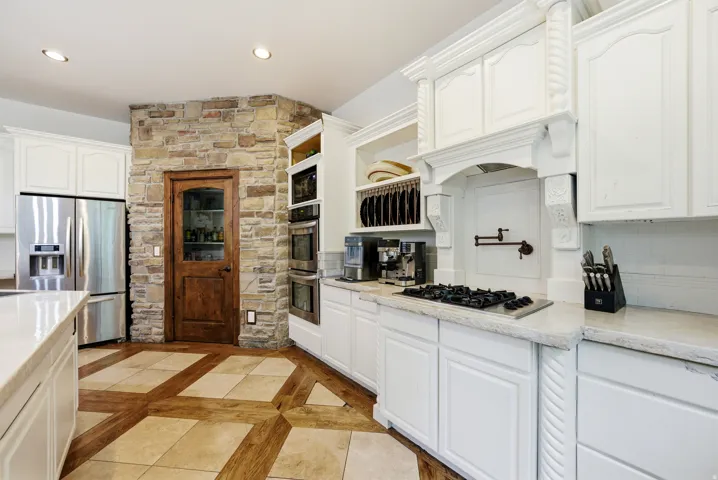 Gourmet kitchen featuring a stone accent wall, decorative range hood, built-in double ovens, and a gas cooktop