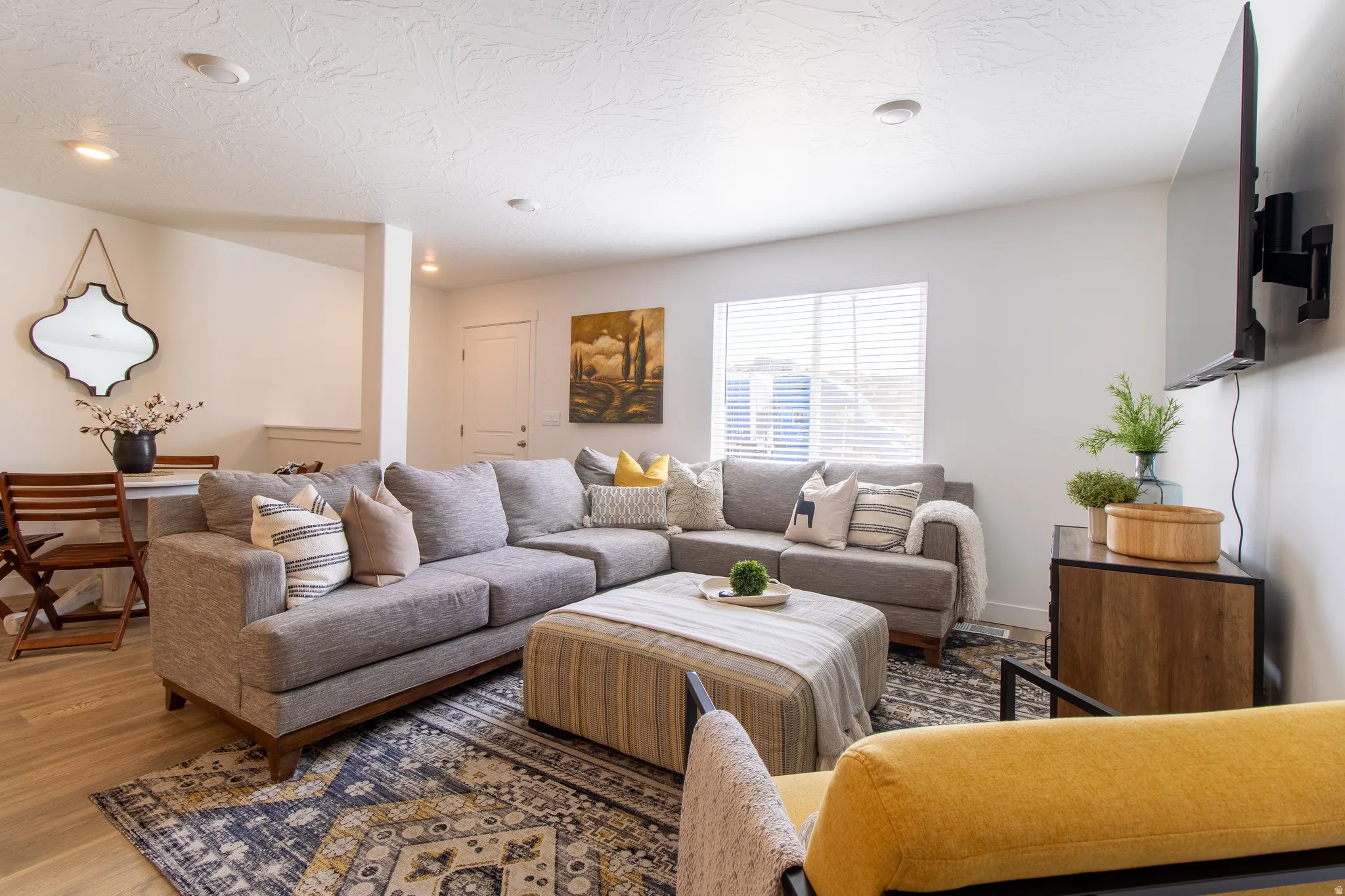 Bright open-concept living space featuring premium laminate flooring, recessed lighting, and a large window with vinyl blinds that brings in plenty of natural light