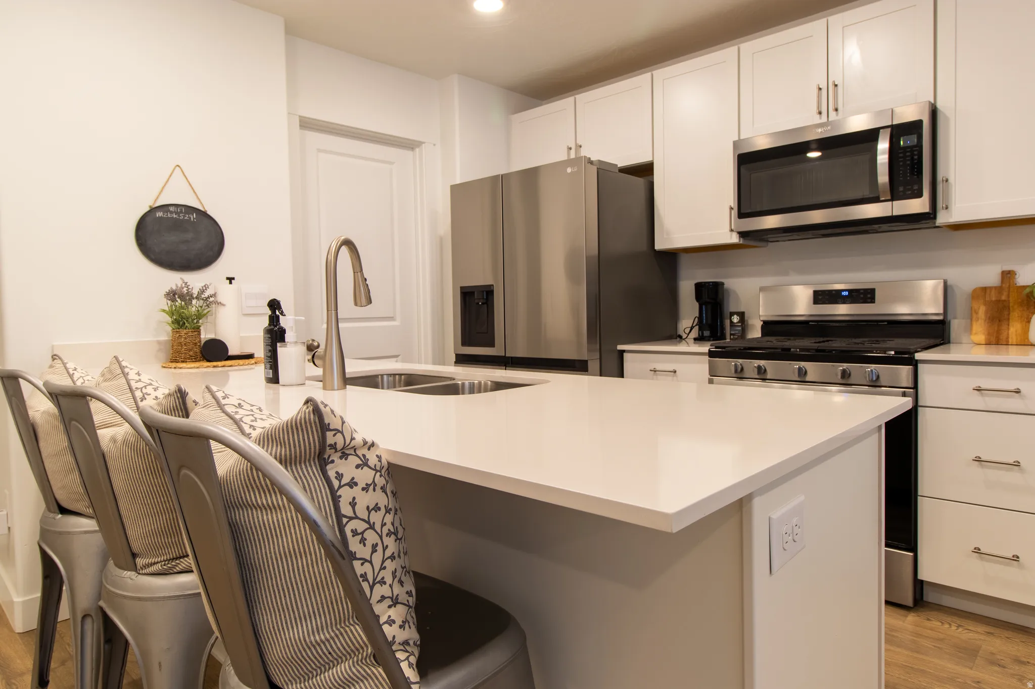 Contemporary kitchen featuring white cabinetry, quartz countertops, stainless steel appliances, countertop seating, and premium laminate flooring