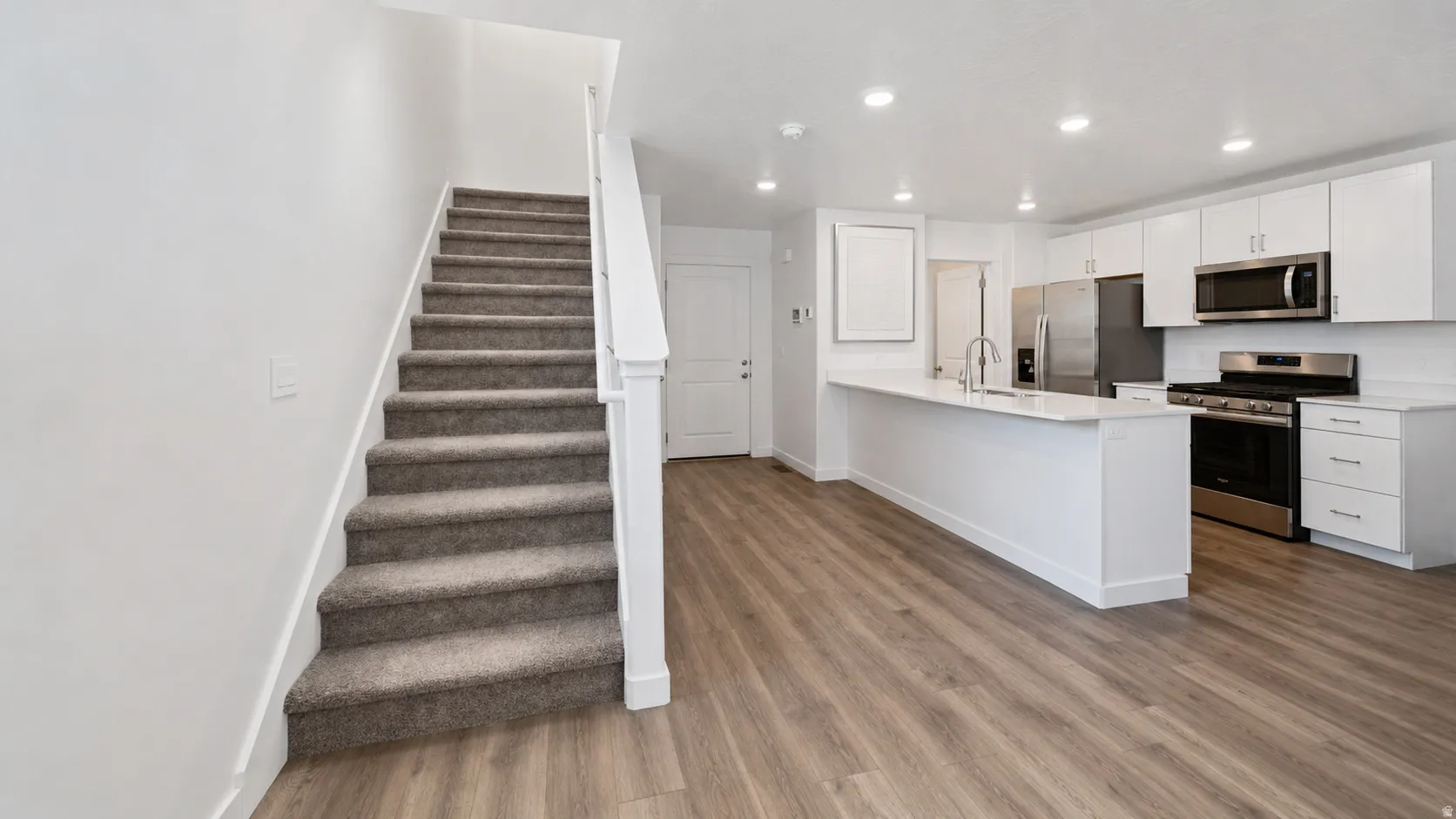 Open-concept living space with premium laminate flooring, a contemporary kitchen, white cabinetry, stainless steel appliances, and bar seating