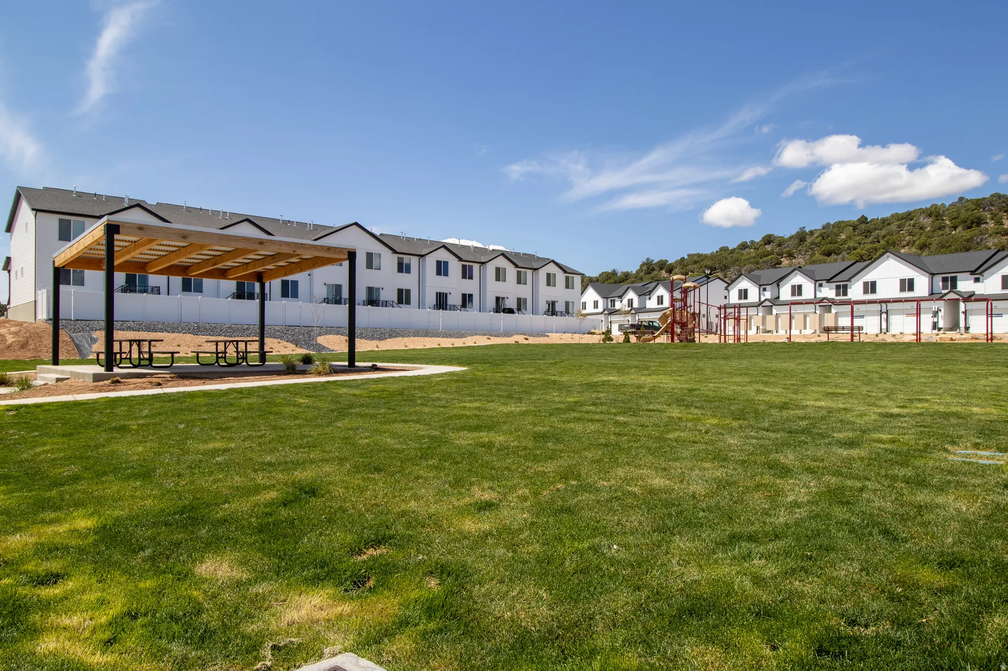 Expansive green space featuring a modern pergola with picnic tables, a children's play structure, and mountainous terrain in the background