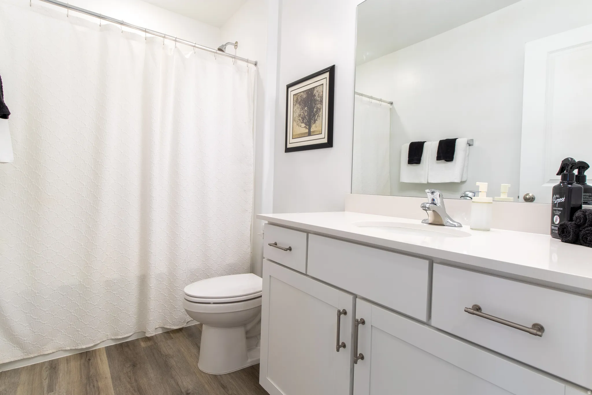 Bathroom featuring an extensive quartz countertop,  chrome hardware, white cabinets, large mirror,  premium laminate flooring