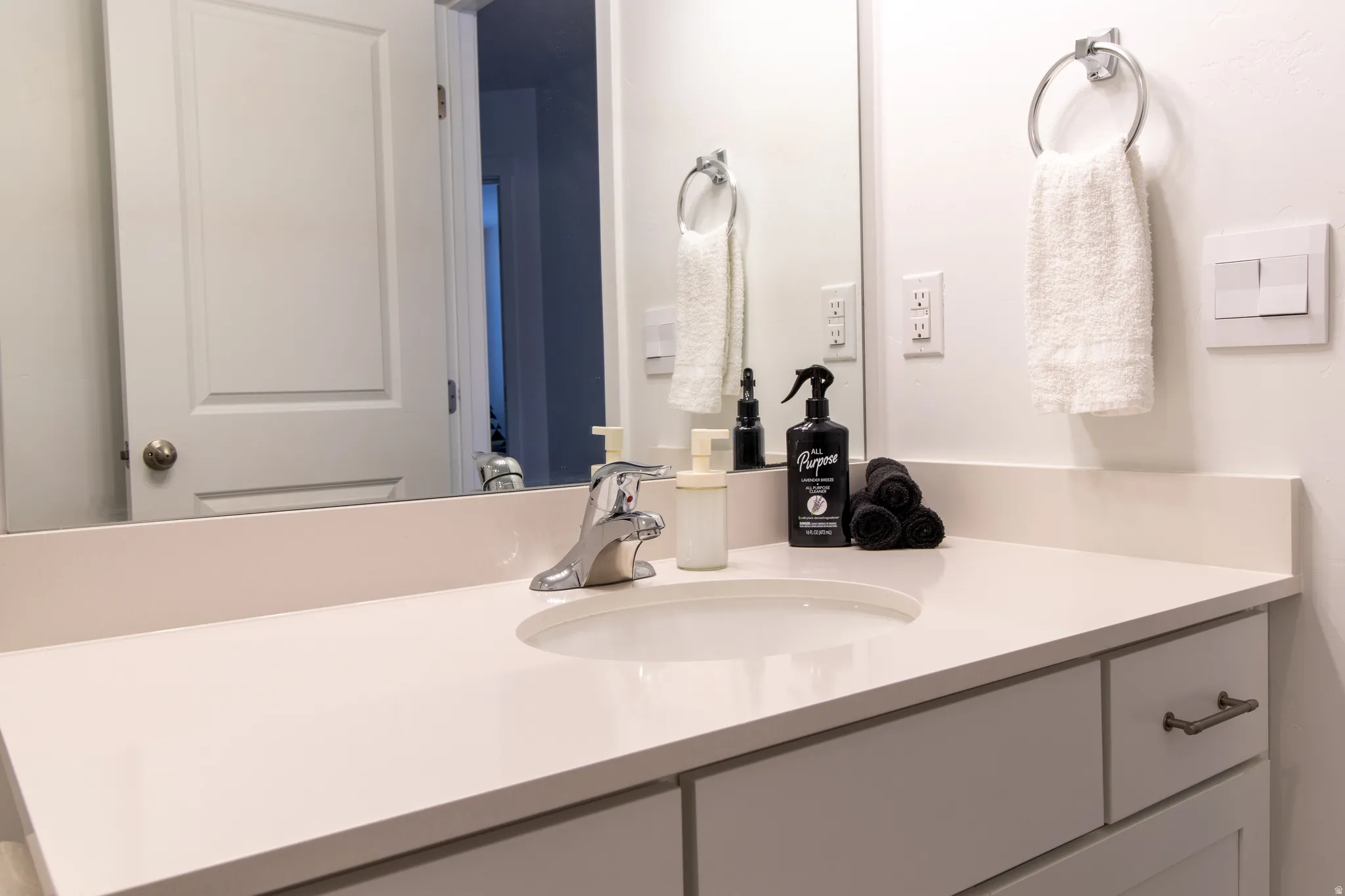 Bathroom featuring an extensive quartz countertop,  chrome hardware, white cabinets, large mirror,  premium laminate flooring