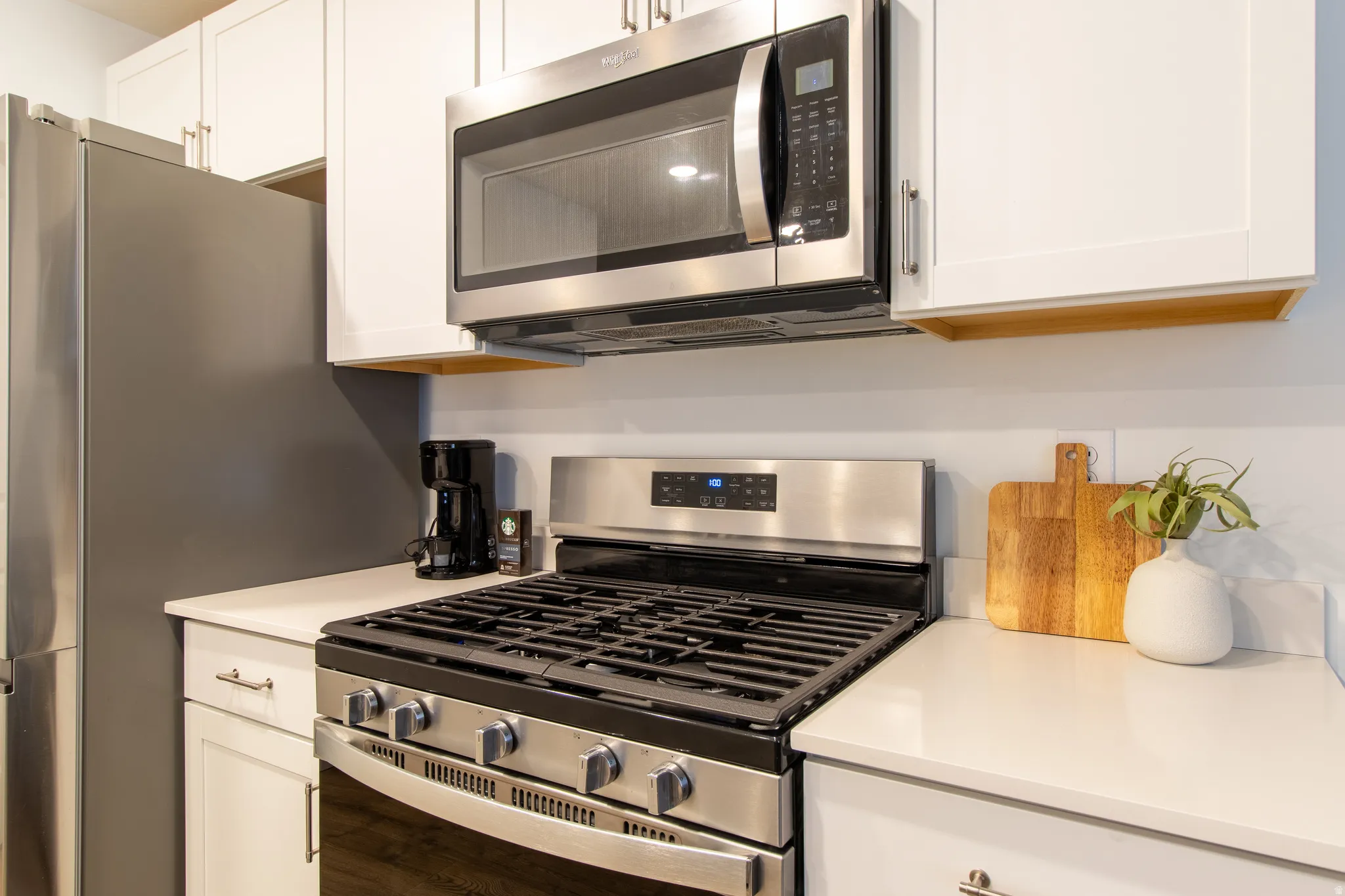 Stainless steel gas range with coordinating microwave, white shaker-cabinetry, quartz countertops, and a stainless steel refrigerator