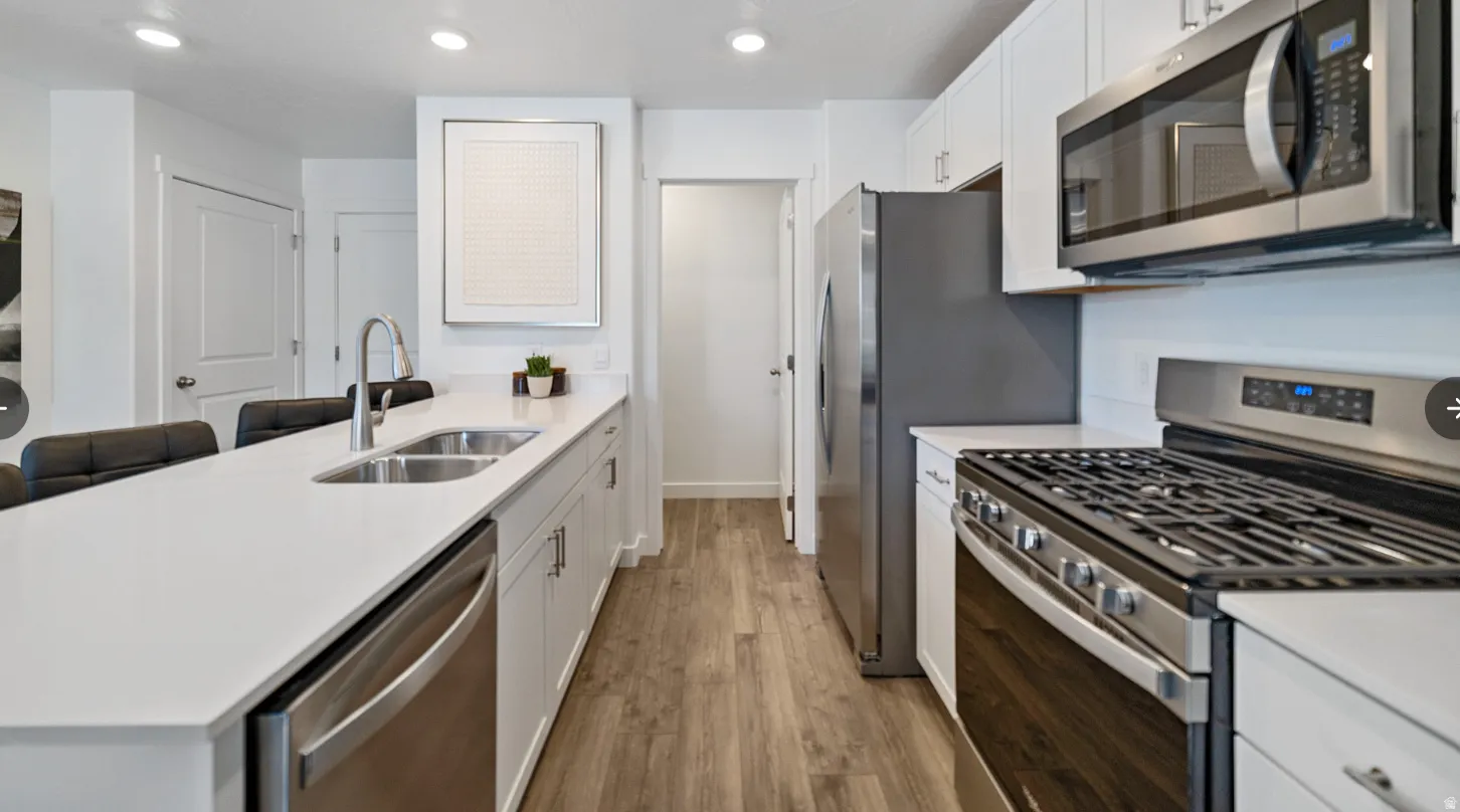 Modern kitchen featuring  quartz countertops, breakfast bar, stainless steel appliances, large pantry, recessed lighting, and premium laminate flooring