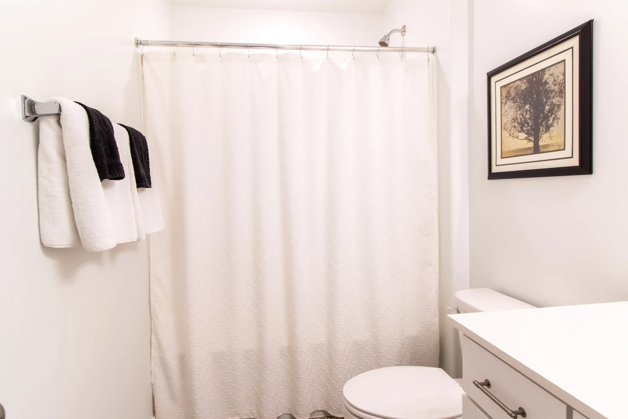 Bathroom featuring an extensive quartz countertop,  chrome hardware, white cabinets, large mirror,  premium laminate flooring