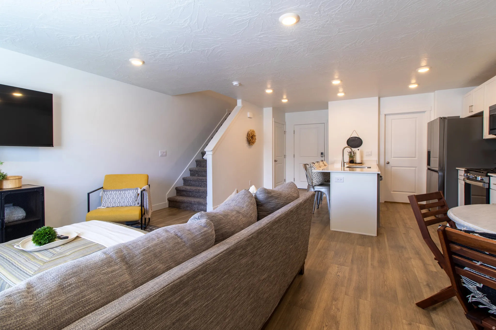 Bright open-concept living space featuring premium laminate flooring, recessed lighting, and a large window with blinds that brings in plenty of natural light