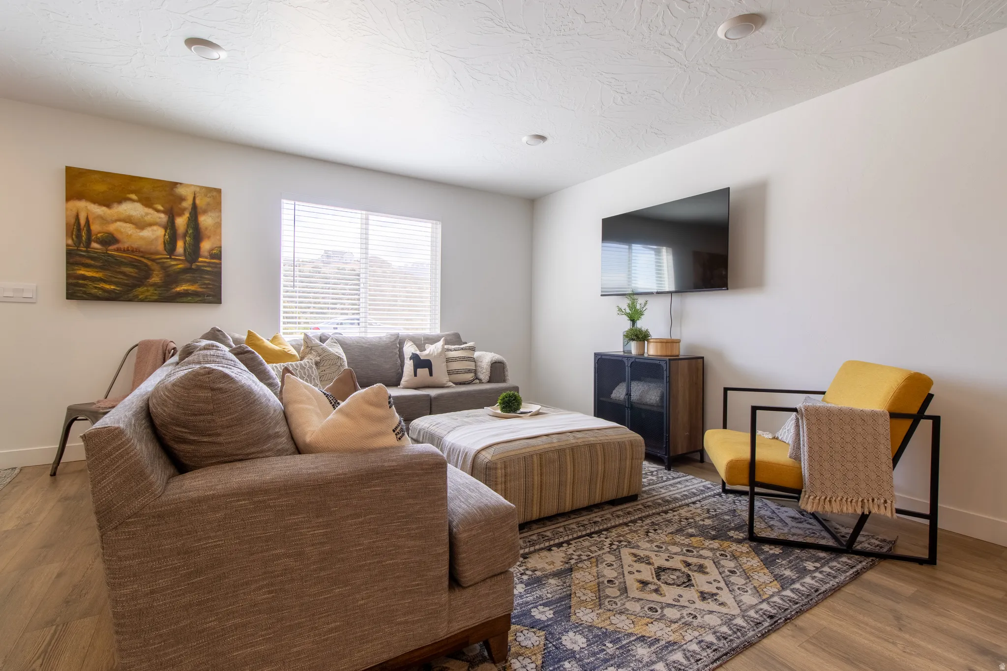 Bright open-concept living space featuring premium laminate flooring, recessed lighting, and a large window with blinds that brings in plenty of natural light