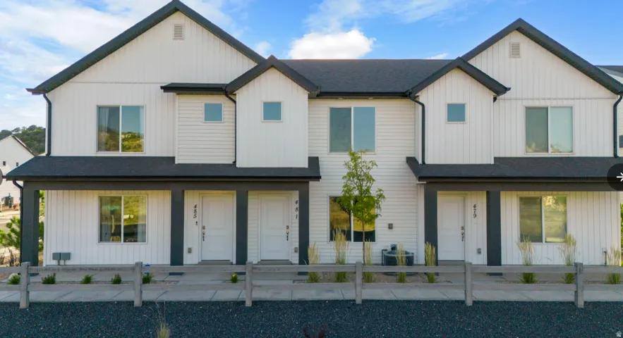 Modern townhome exterior featuring white siding with dark trim, a dark-pitched roof, and a covered entryway. Garage is in the back of the townhome