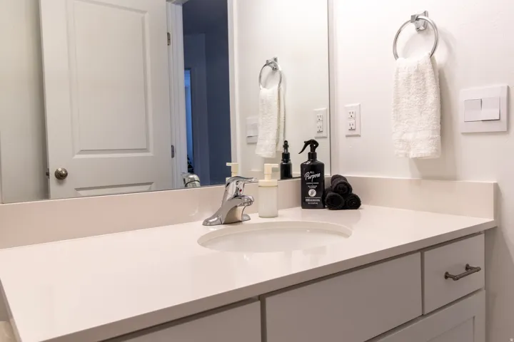 Bathroom featuring an extensive quartz countertop,  chrome hardware, white cabinets, large mirror,  premium laminate flooring
