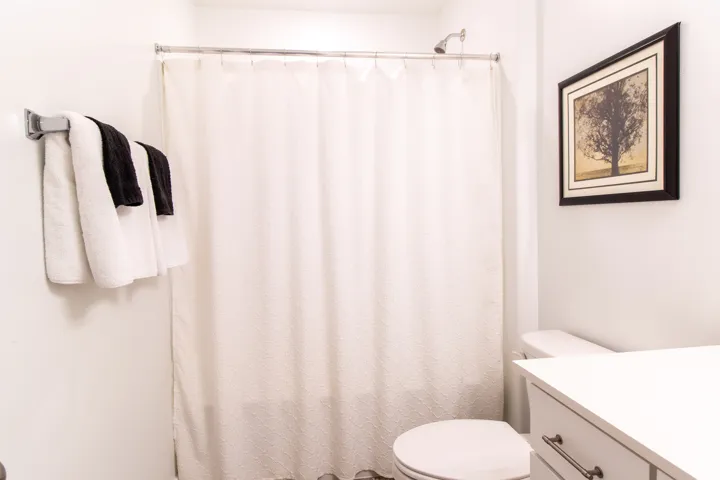 Bathroom featuring an extensive quartz countertop,  chrome hardware, white cabinets, large mirror,  premium laminate flooring
