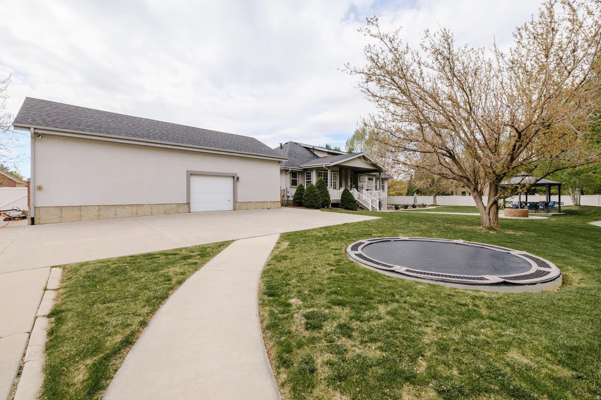 View of front facade featuring a trampoline, a shingled roof, driveway, and stucco siding