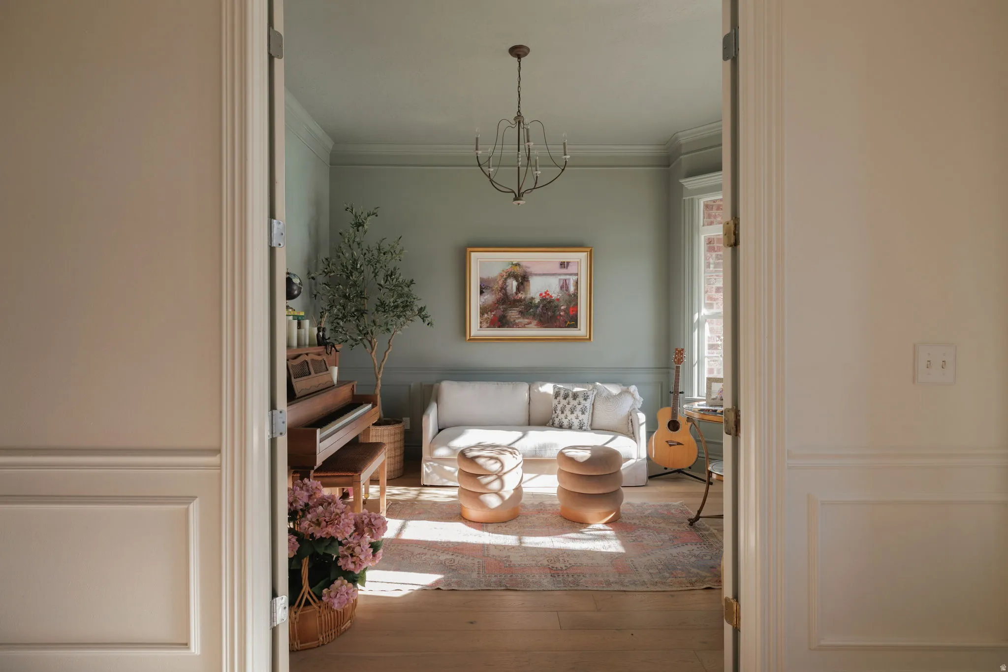 Living room with a wainscoted wall, ornamental molding, a decorative wall, light wood-style floors, and hanging lights