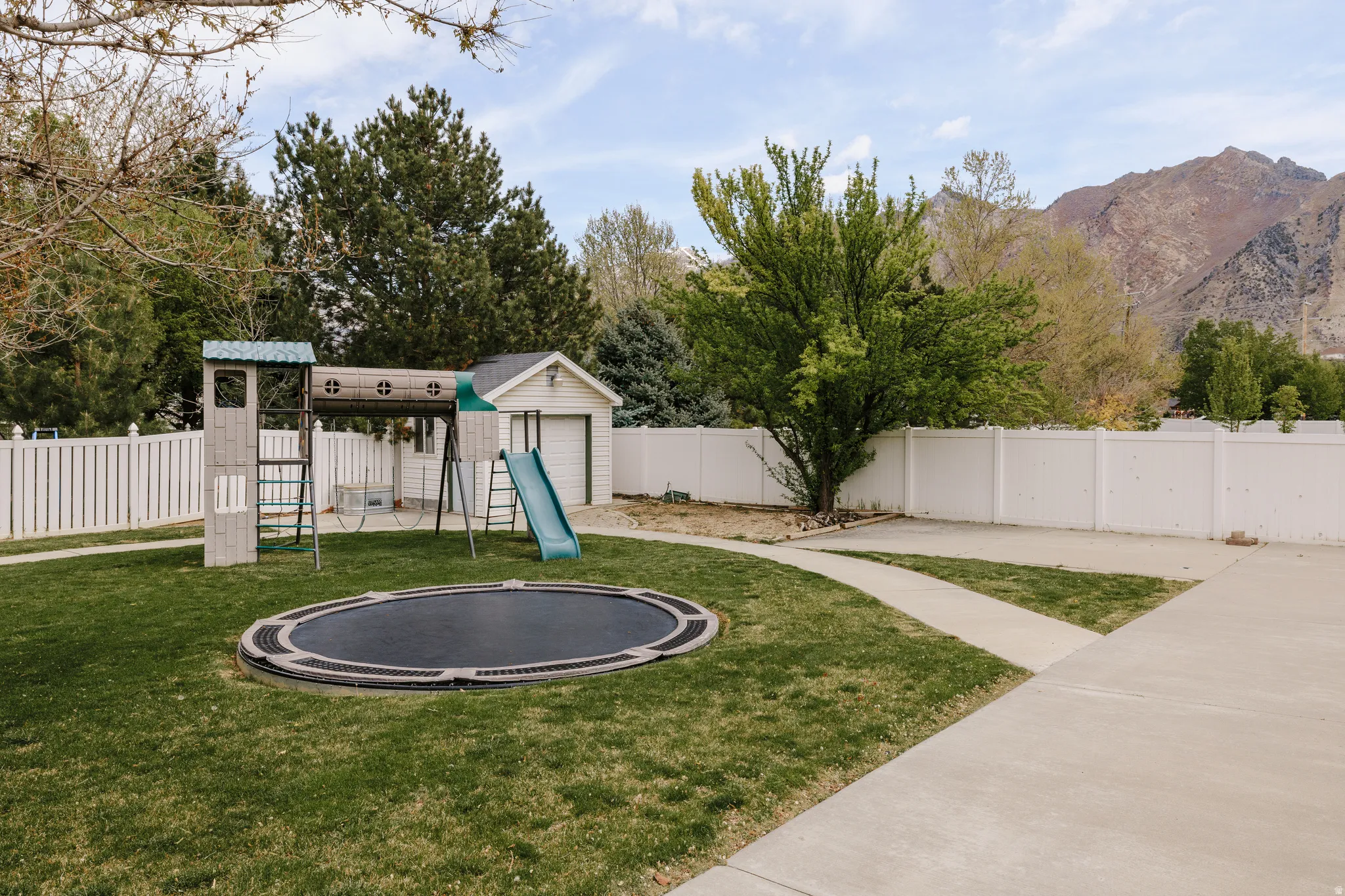 Fenced backyard featuring a playground, a trampoline, and a mountain view