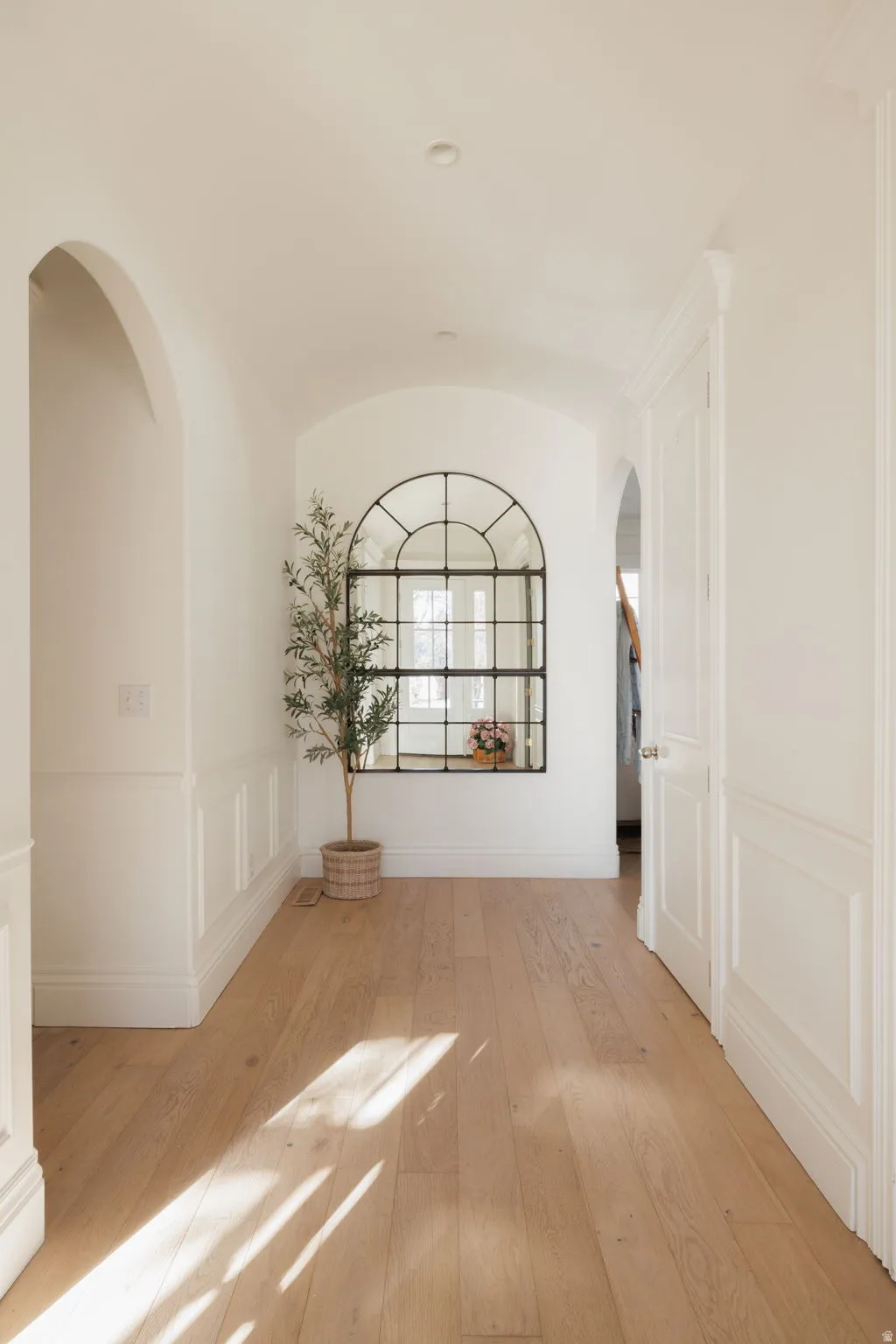 Unfurnished room featuring a decorative wall, a barrel ceiling, arched walkways, light wood-style flooring, and a wainscoted wall