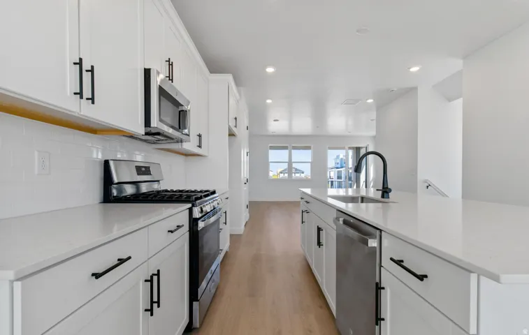Modern kitchen featuring white cabinetry, stainless steel appliances, a gas range, white subway tile backsplash, and light-tone wood-finish flooring