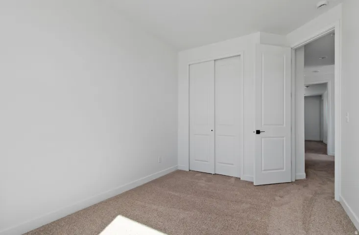 Carpeted interior room featuring white walls, white trim, a solid panel door with dark hardware, and bi-fold closet doors
