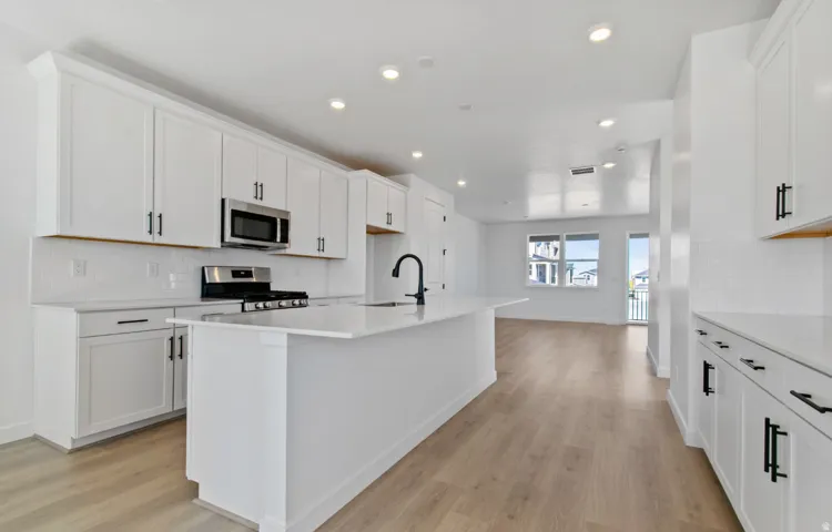 Modern kitchen featuring white cabinetry, a center island with sink, stainless steel appliances, and wood-finish flooring