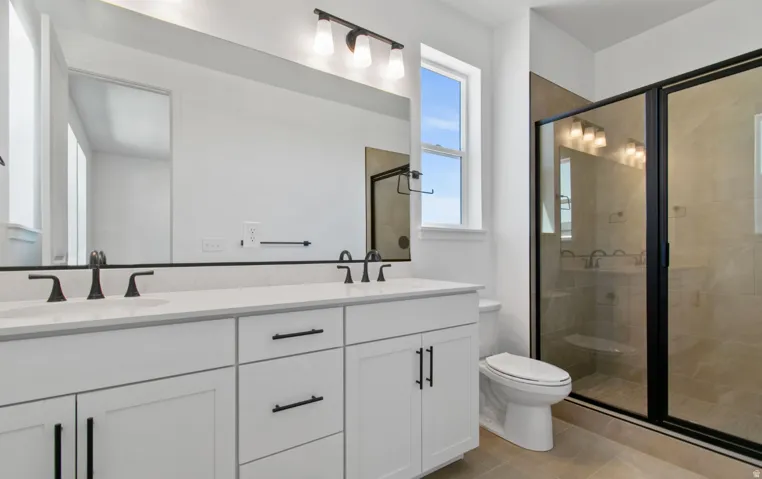Double vanity featuring white cabinetry, matte black hardware, and an expansive mirror