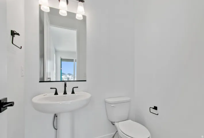 Pedestal sink with matte black faucet, wall-mounted mirror, and overhead vanity lighting