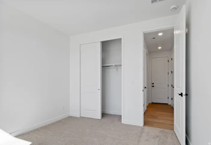 Carpeted room featuring a double-door closet with a hanging rod, white walls, and a white baseboard