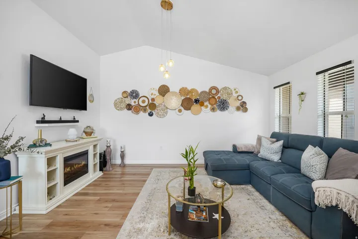 Spacious living area featuring vaulted ceilings, wood-finish flooring, and multiple windows with blinds