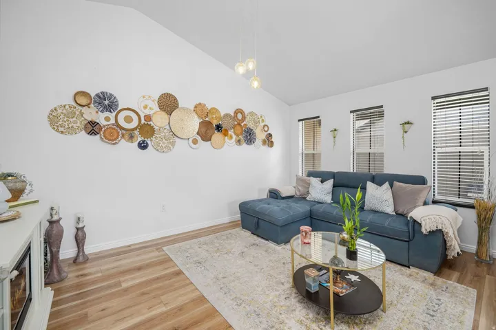Living area featuring vaulted ceilings, wood-finish flooring, and multiple windows with blinds