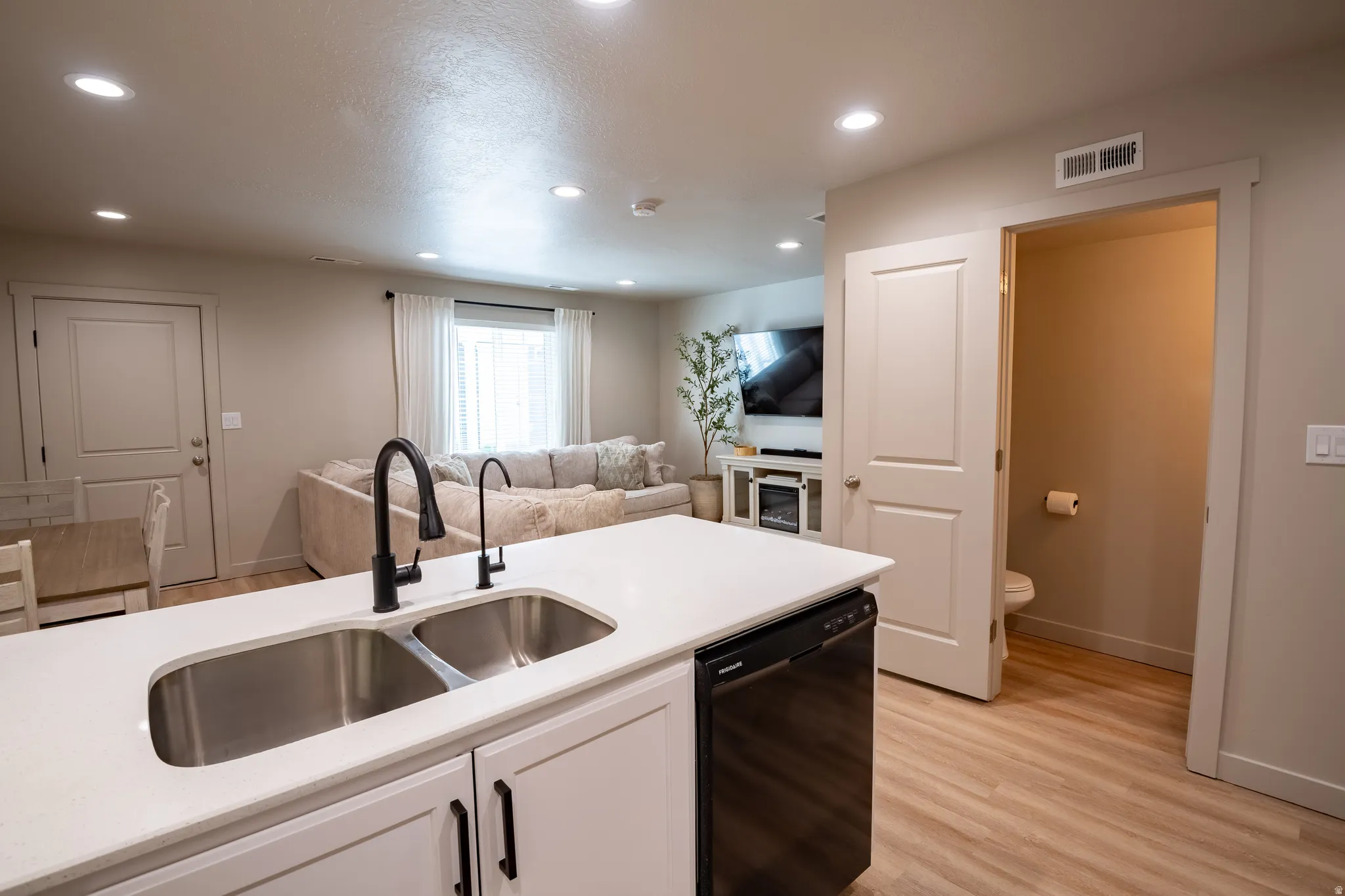 Kitchen island featuring a double basin stainless steel sink with matte black fixtures, white countertop, and integrated dishwasher