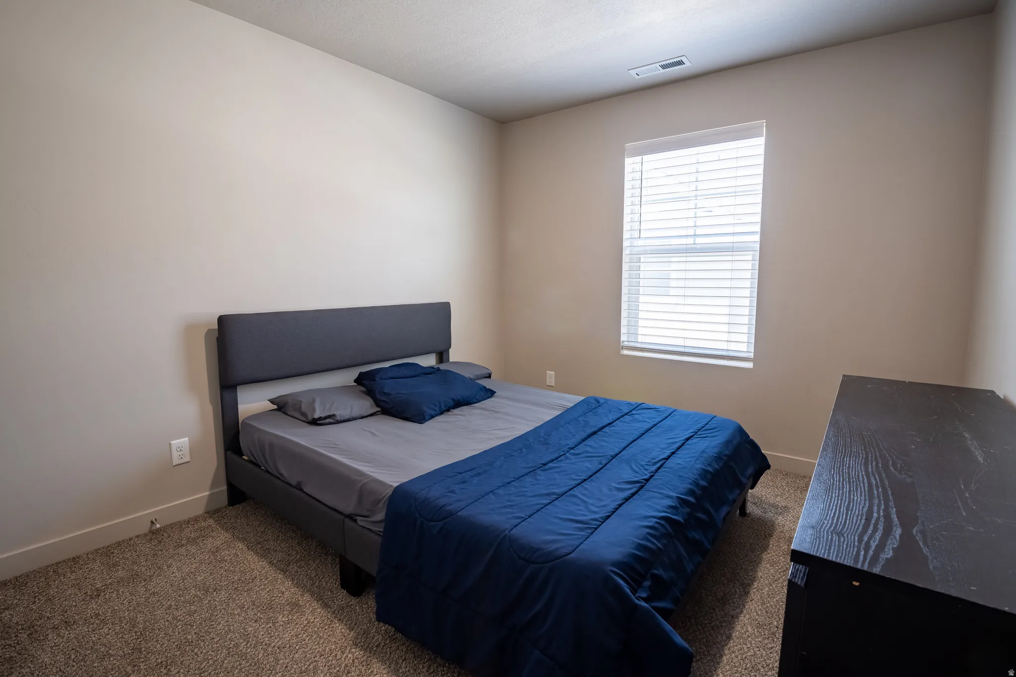 Neutral tone wall paint, window with blinds, recessed ceiling vent, low-pile carpeting, and white baseboards