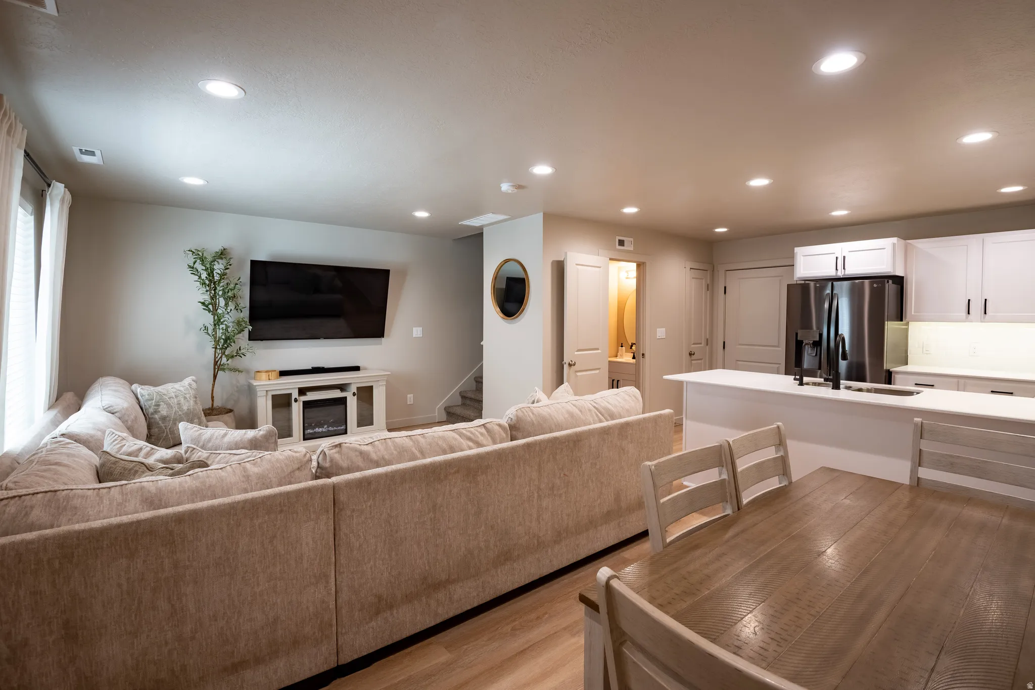 Open-concept living space featuring wood-finish flooring, recessed lighting, and a white entertainment console with an electric fireplace