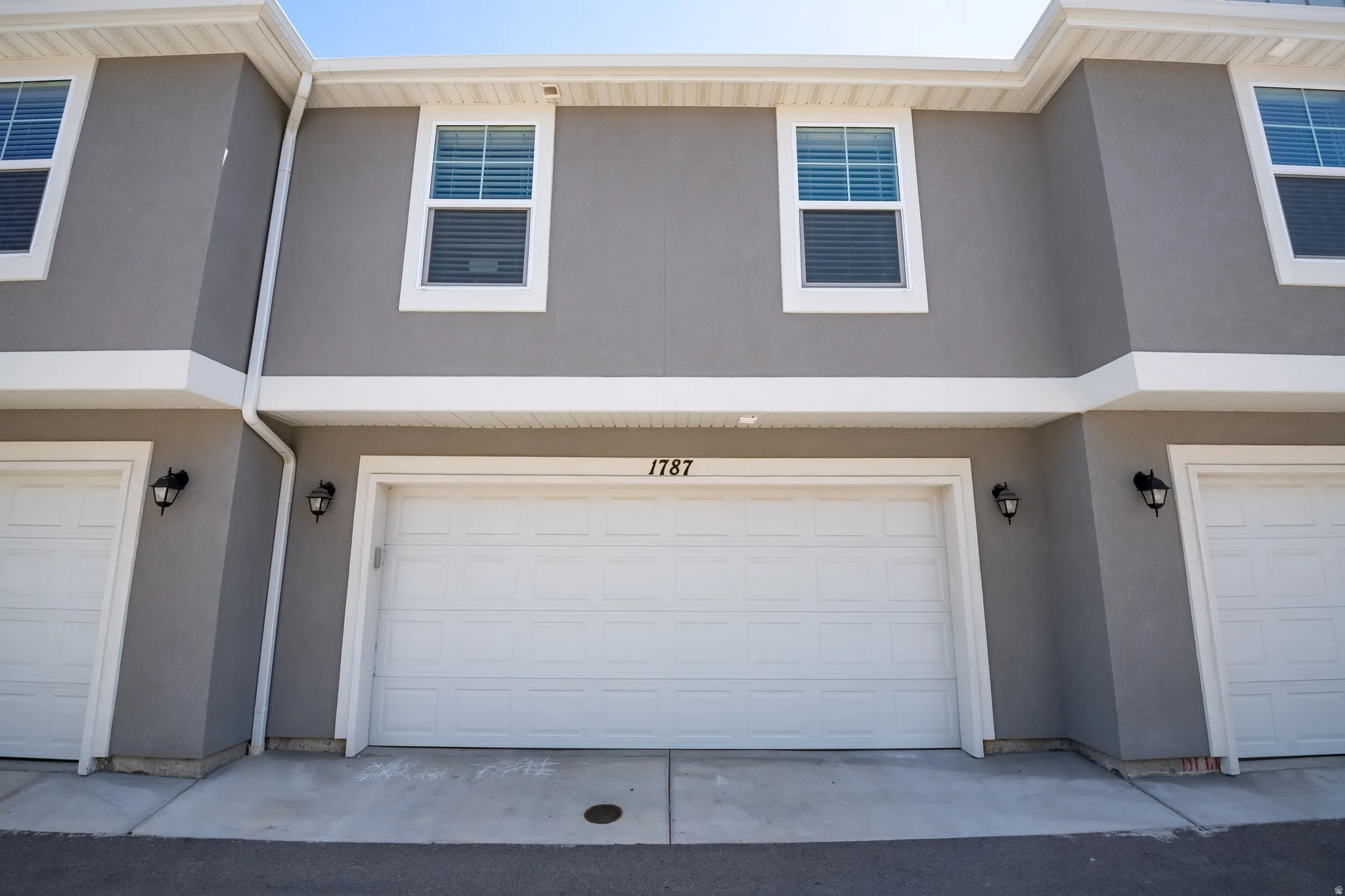 Gray stucco exterior with white trim, featuring a prominent two-car garage with white paneled doors