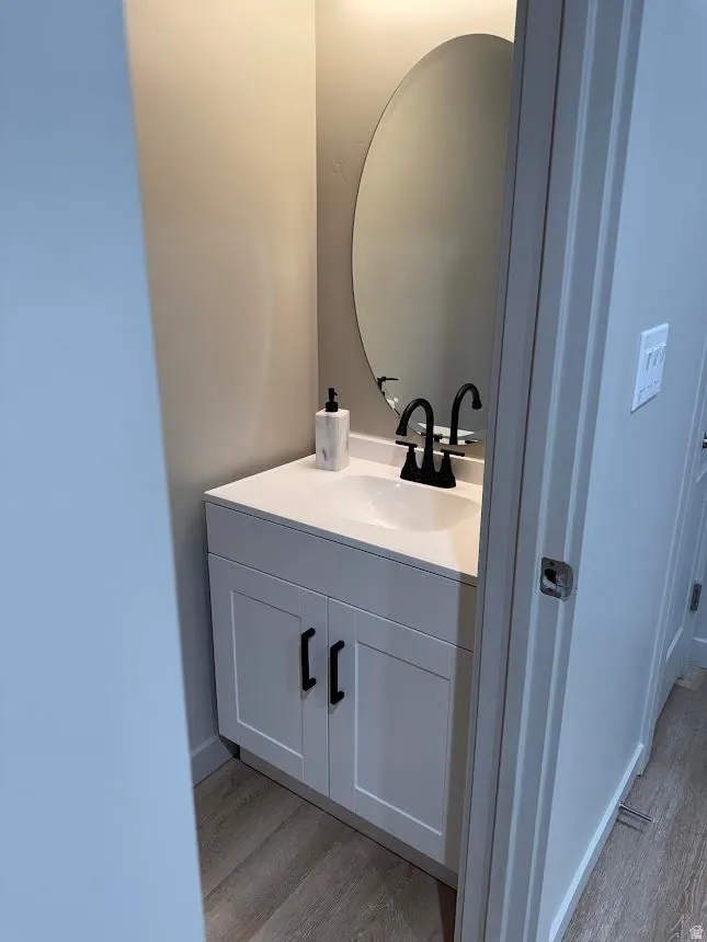 Vanity area featuring a white cabinet base, single-basin sink, black faucet, and an oval mirror