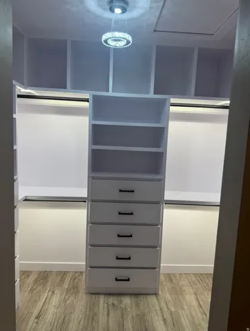 Custom closet system featuring multiple open shelves, built-in drawers with black hardware, and hanging rods