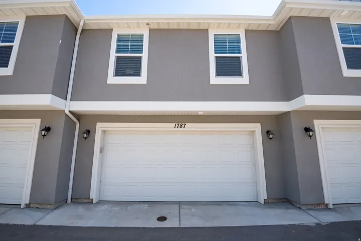 Gray stucco exterior with white trim, featuring a prominent two-car garage with white paneled doors