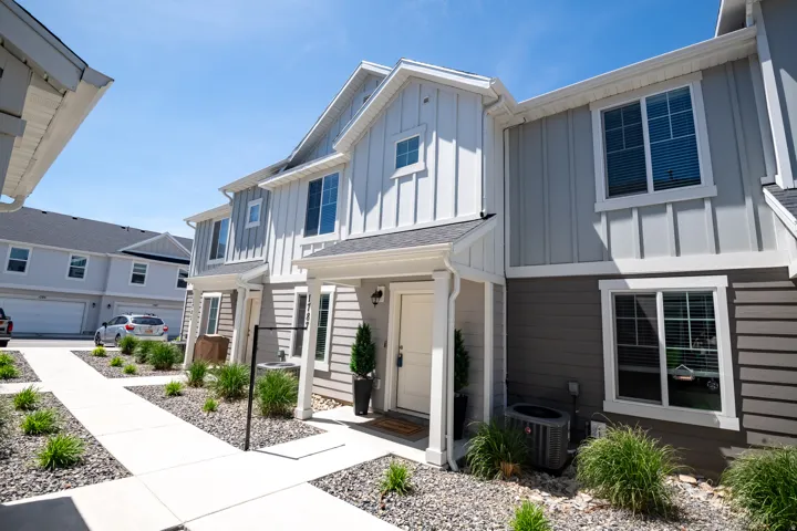 Two-story townhome featuring a covered entry, vertical and horizontal siding, and multiple windows with white trim
