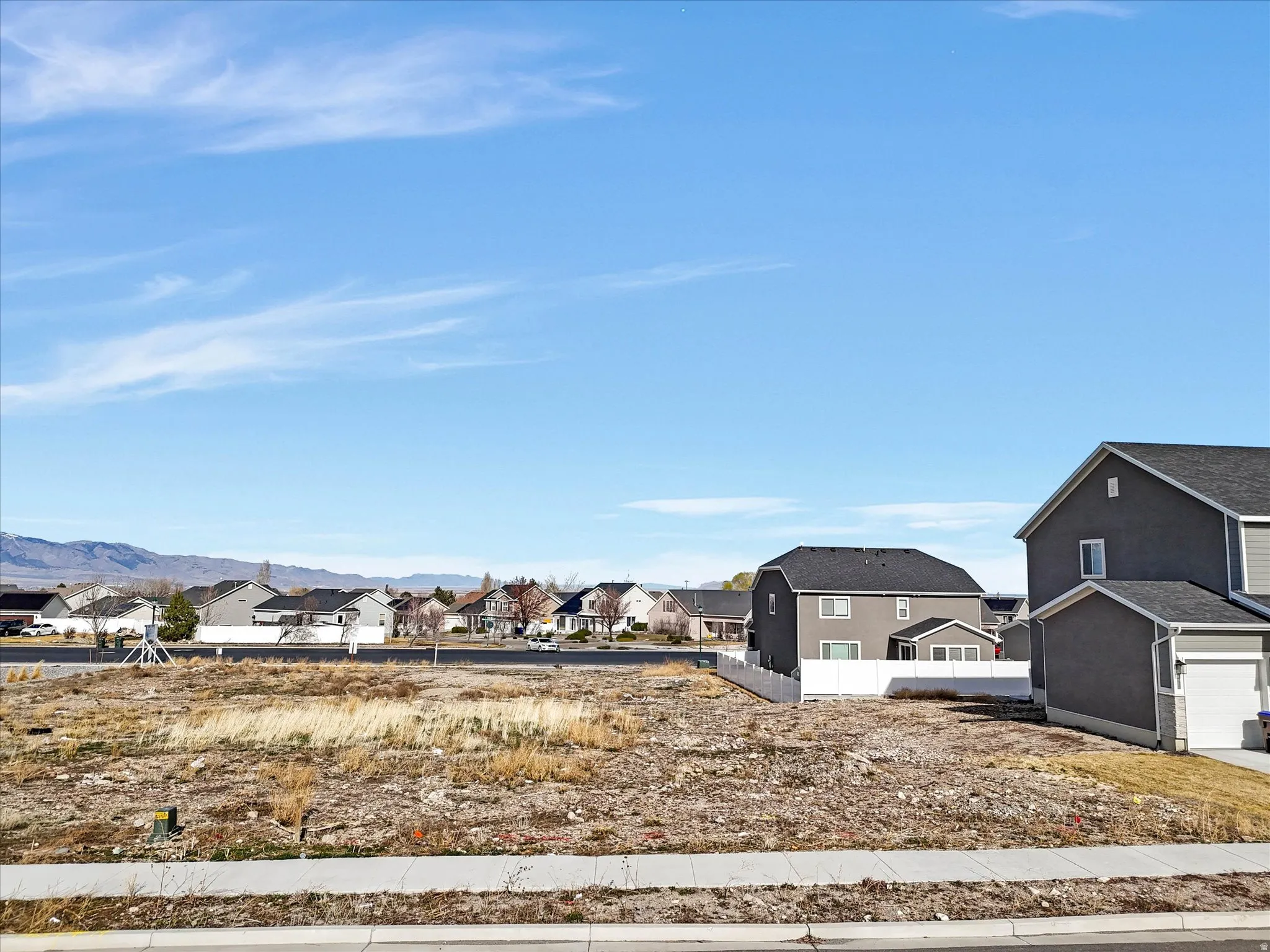 Expansive undeveloped lot featuring a concrete sidewalk and a street with curb