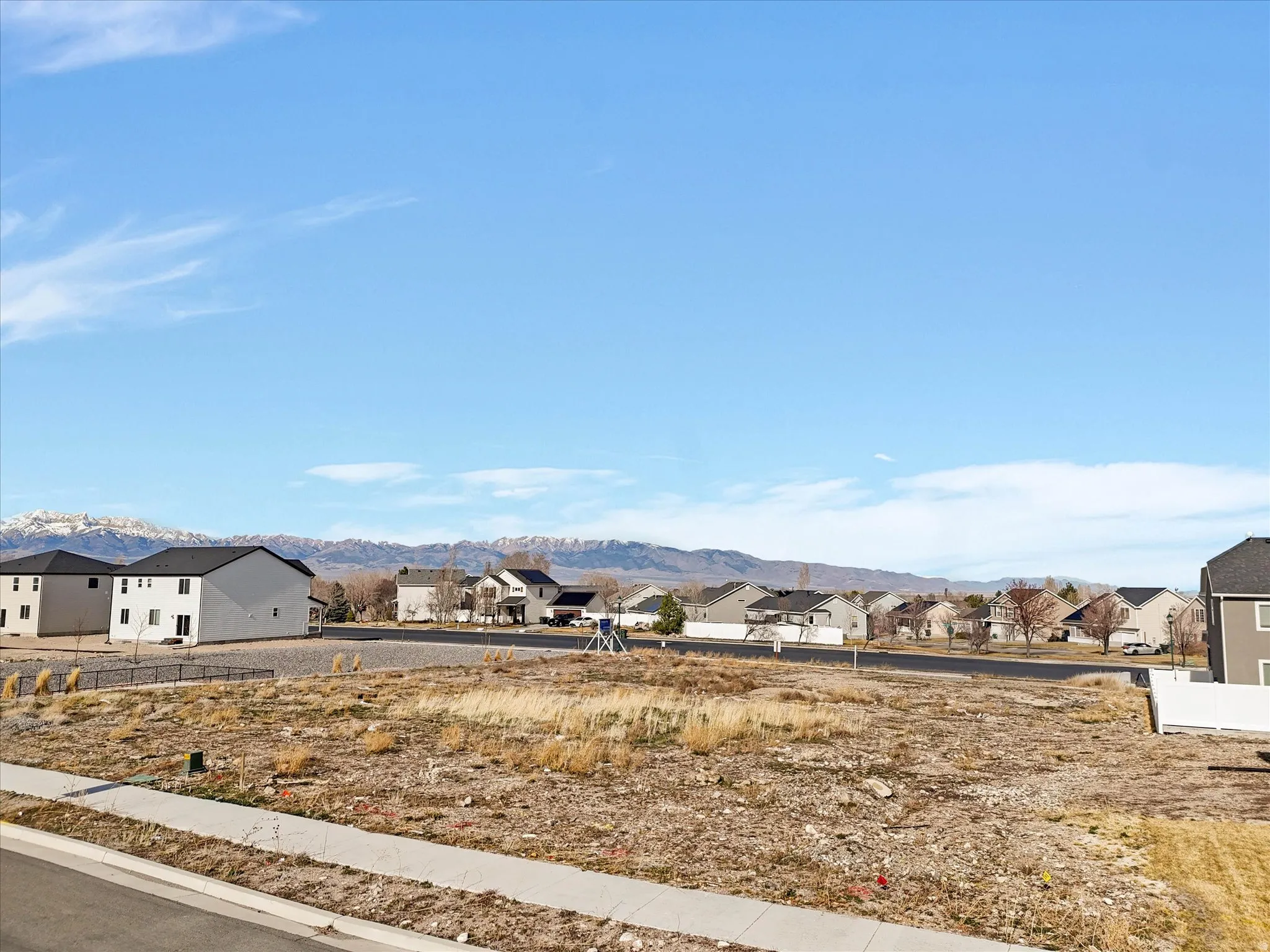 Unfinished lot with sidewalk frontage, surrounded by existing residential properties, and distant mountain scenery