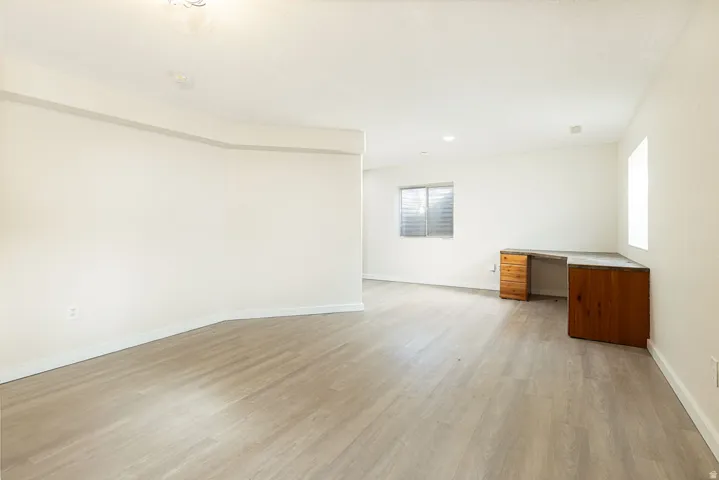 Spacious room featuring light wood-finish flooring, recessed lighting, and a built-in wood desk with storage