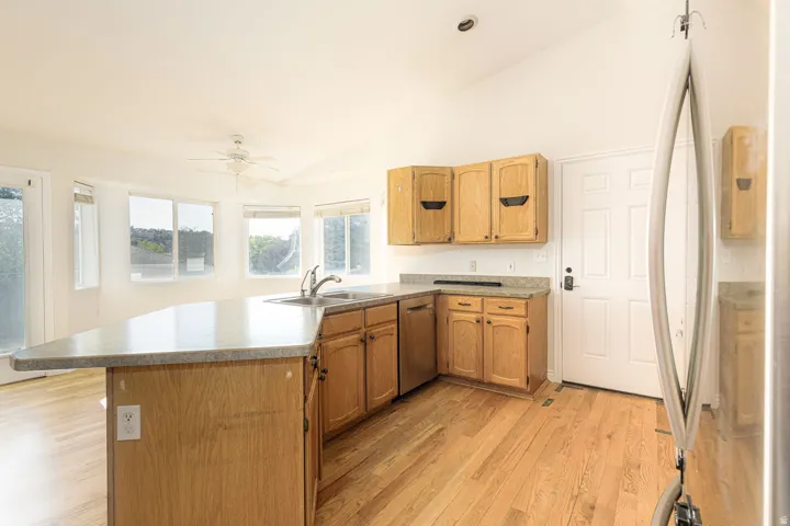 Kitchen area featuring wood-finish flooring, light wood cabinetry, and an integrated kitchen island with a double basin sink