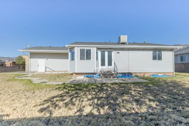 Rear elevation with light gray siding, multiple windows, and a glass-paneled double door leading to a concrete patio