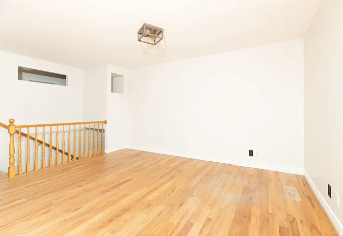 Spacious room featuring wood-finish flooring, white baseboards, and a modern ceiling light fixture