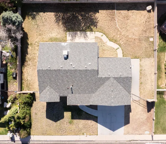 Aerial perspective showcasing a property featuring a multi-pitched shingle roof, a concrete driveway, and a fenced perimeter